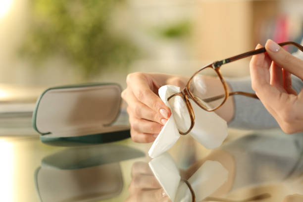 Close up of woman hands cleaning glasses with tissue paper on a desk at home